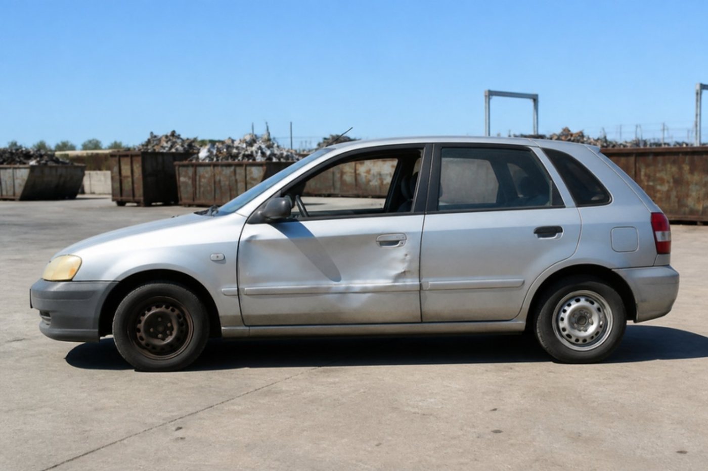 An old silver hatchback parked in a scrap yard